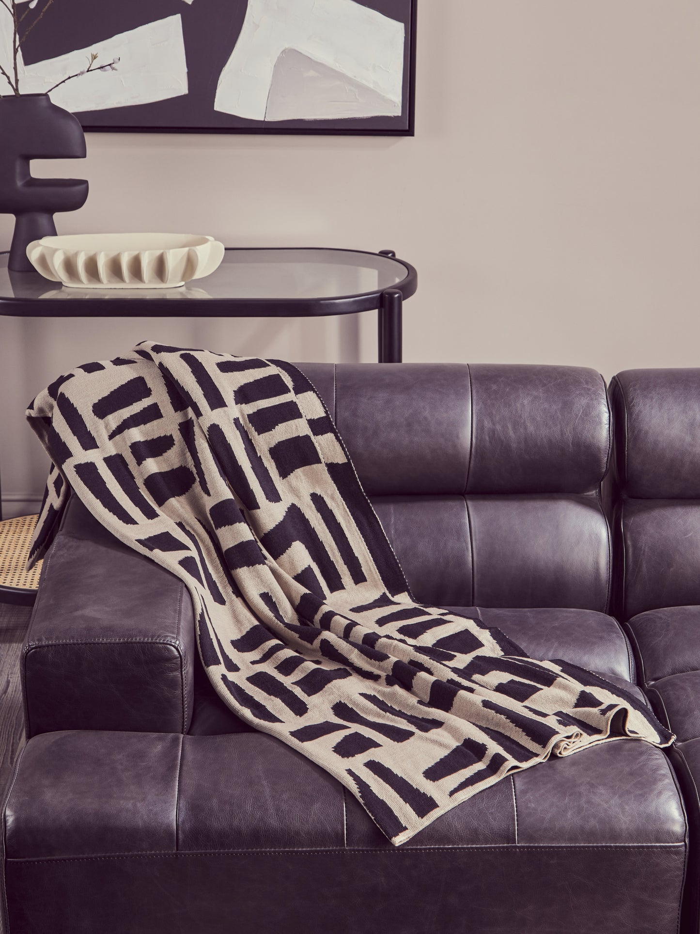 Patterned blanket draped over a dark leather sofa with abstract art in the background.