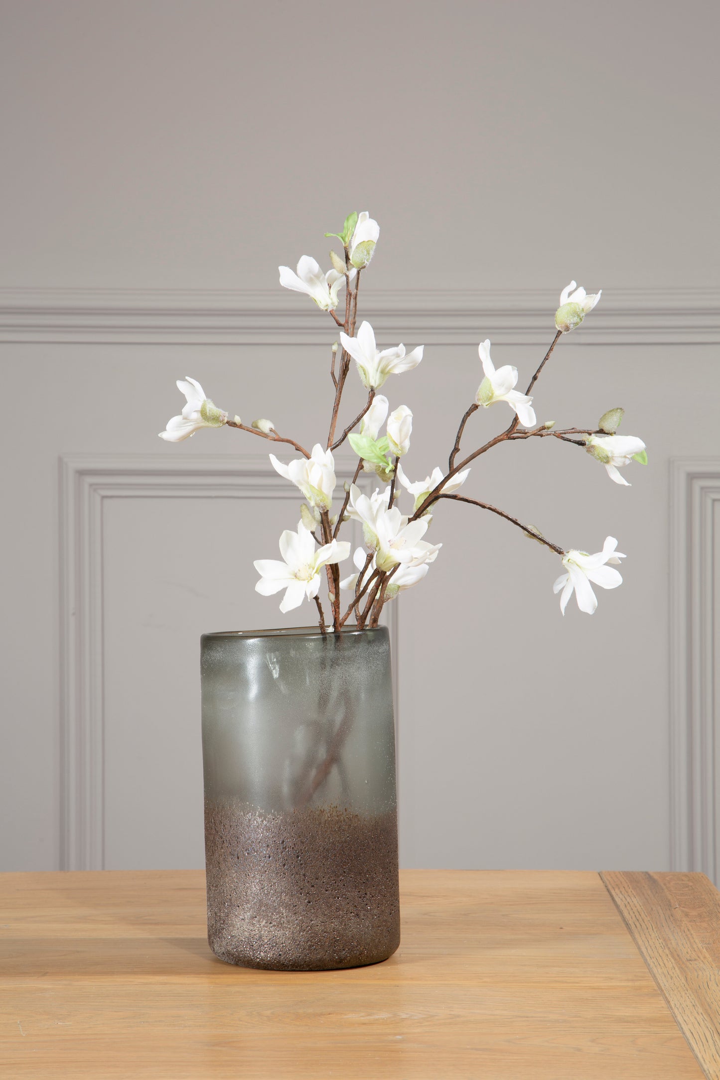 Decorative vase with white flowers on a wooden surface against a gray wall.