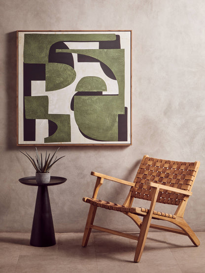 Abstract art piece on a wall above a woven chair and small table.
