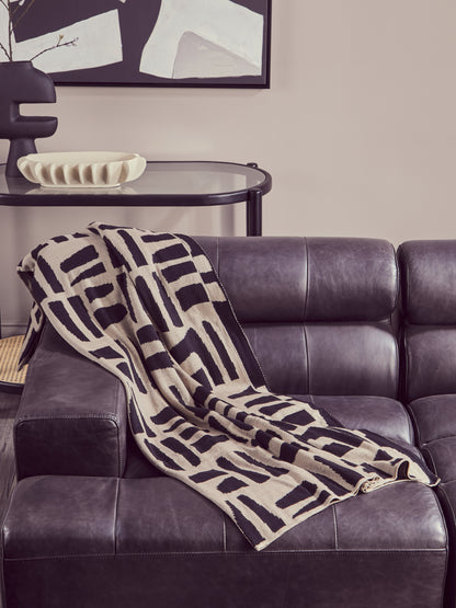 Patterned blanket draped over a dark leather sofa with abstract art in the background.