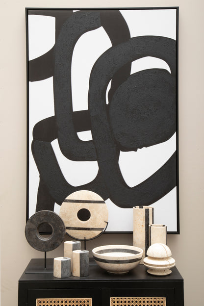 Abstract black and white artwork on a wall with decorative items below.