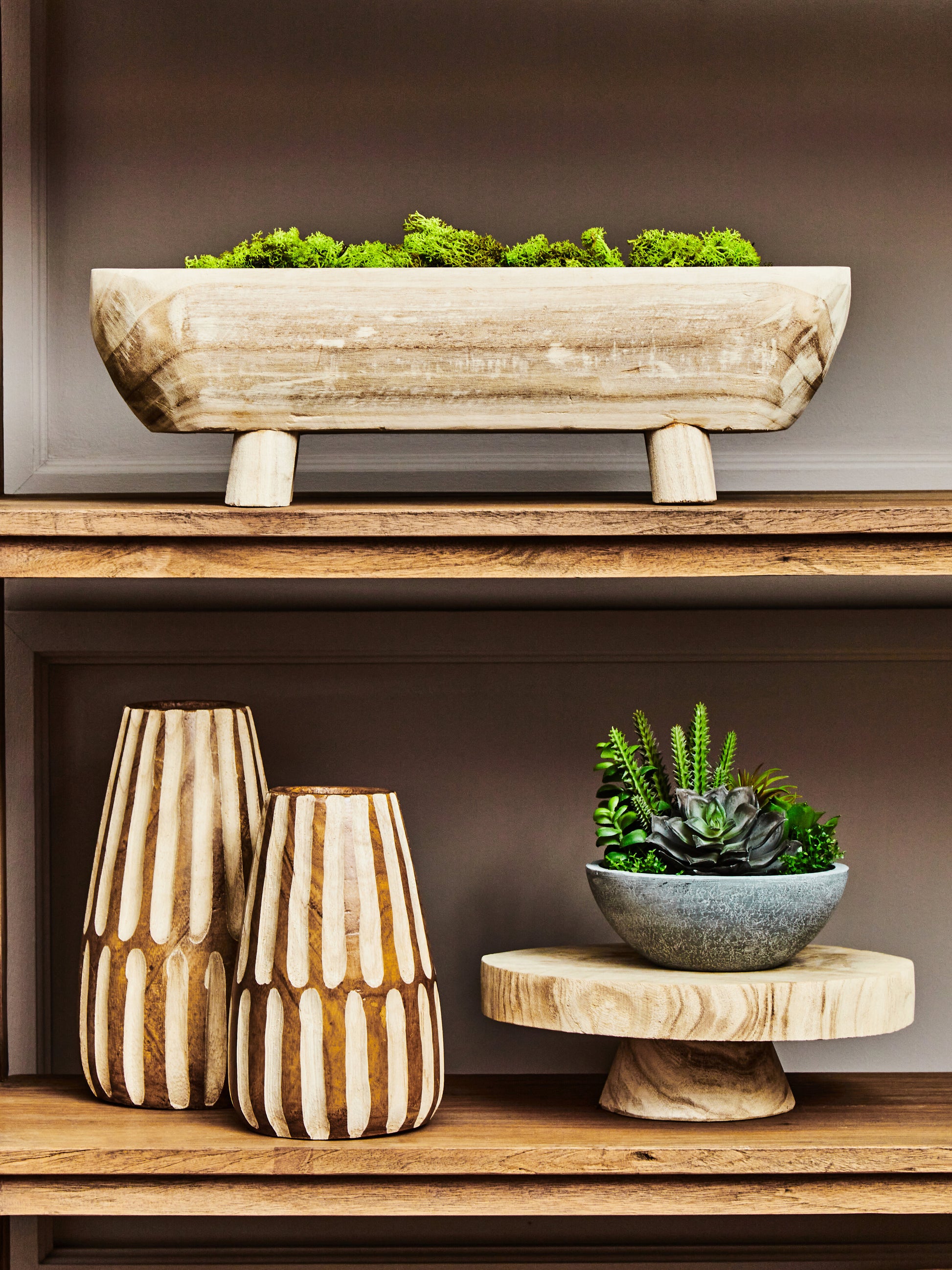 Decorative wooden shelf with vases, a bowl, and plants against a neutral background
