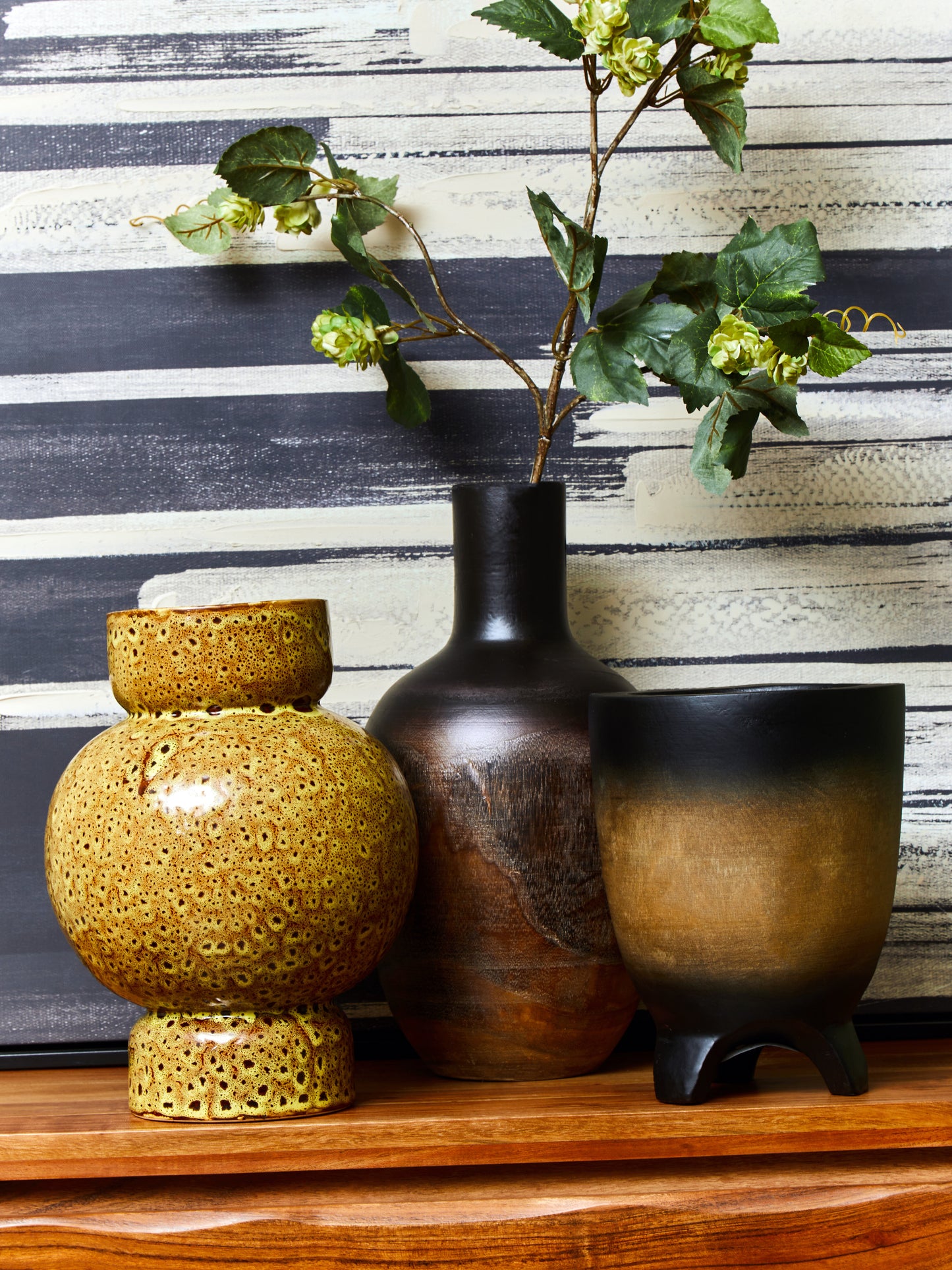 Three ceramic vases on a wooden surface with a striped wall in the background