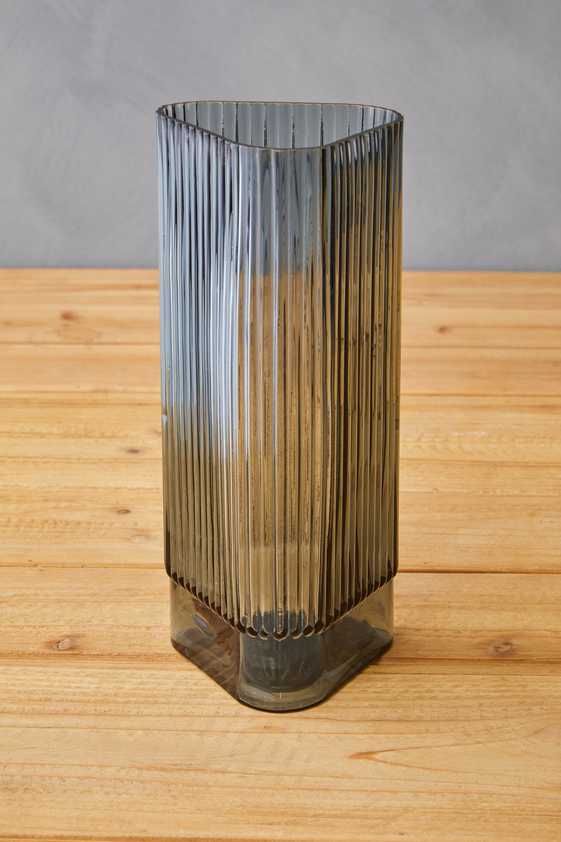 Tall, ribbed glass vase on a wooden surface with a gray background