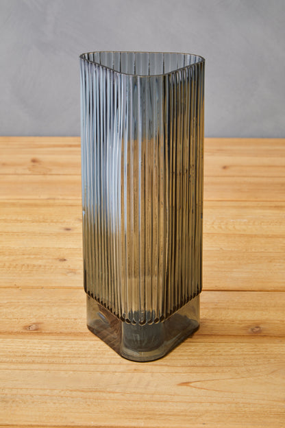 Tall, ribbed glass vase on a wooden surface with a gray background