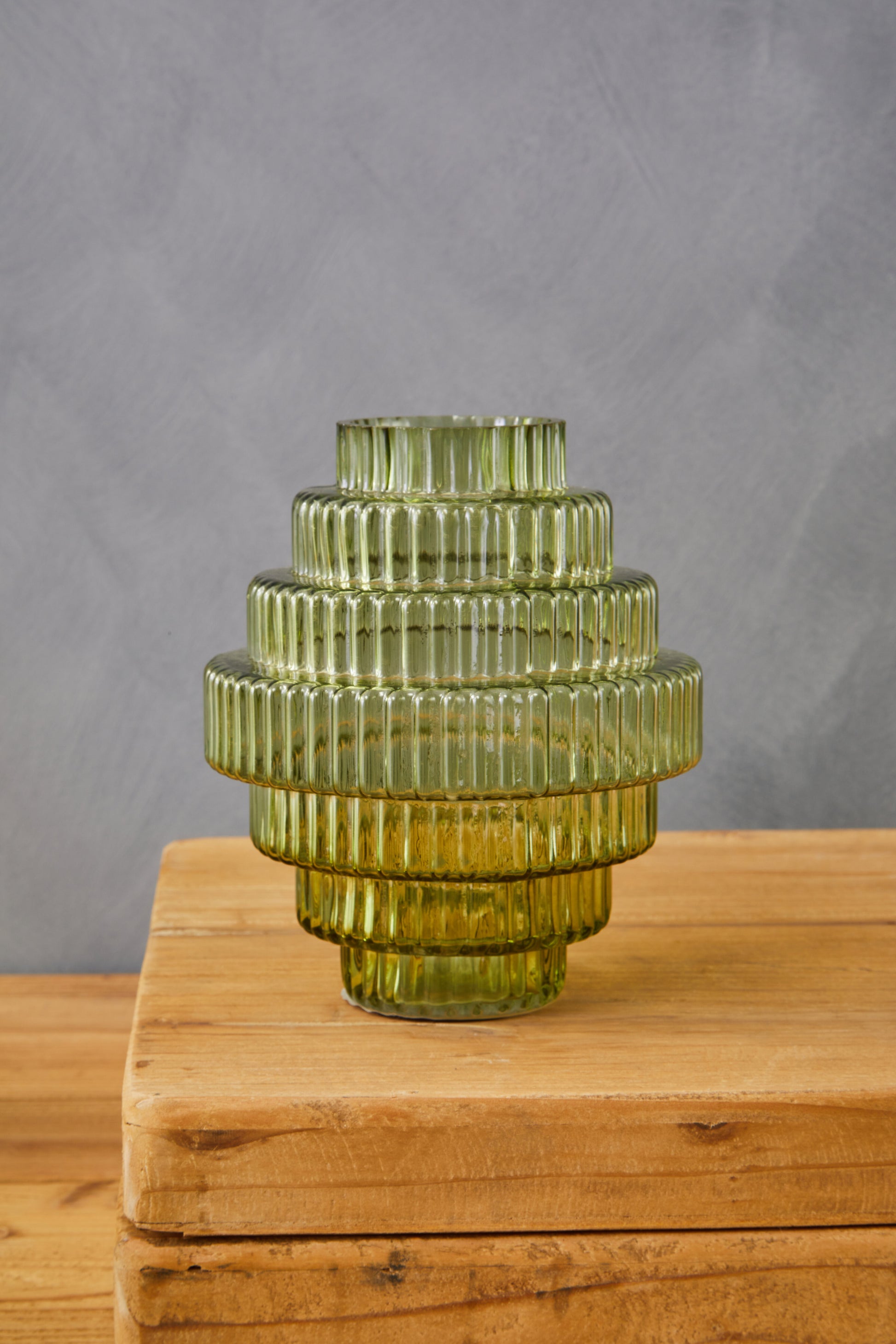 Green glass vase with ribbed texture on a wooden surface against a gray background