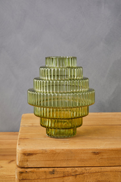 Green glass vase with ribbed texture on a wooden surface against a gray background