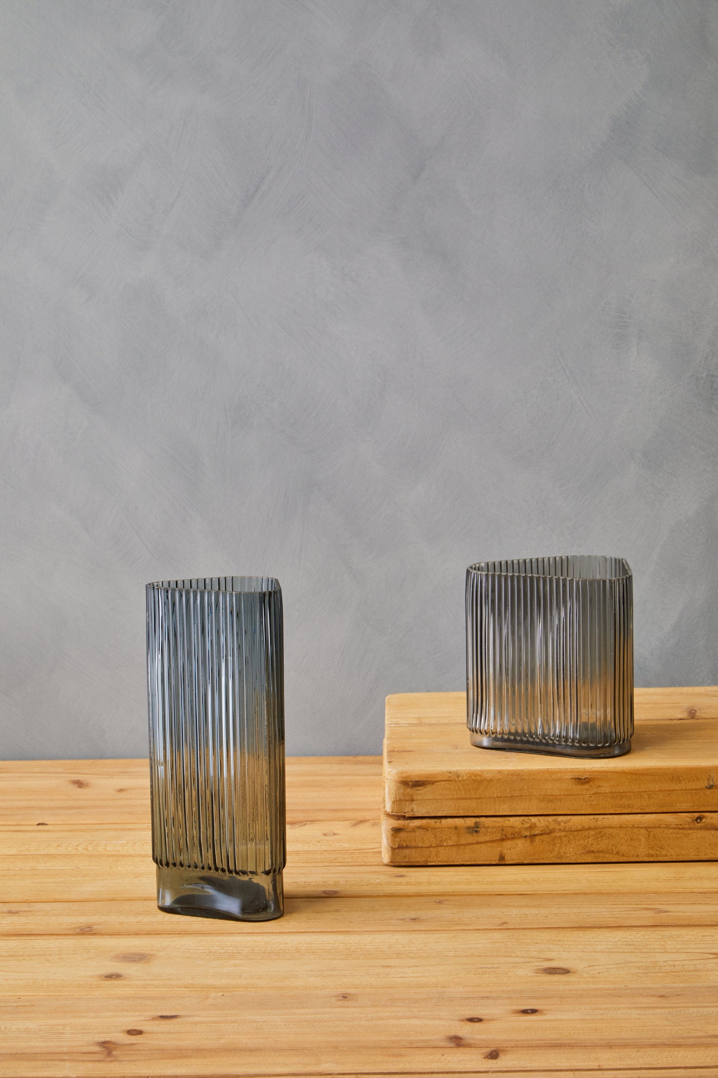 Two ribbed glass vases on a wooden surface with a gray background