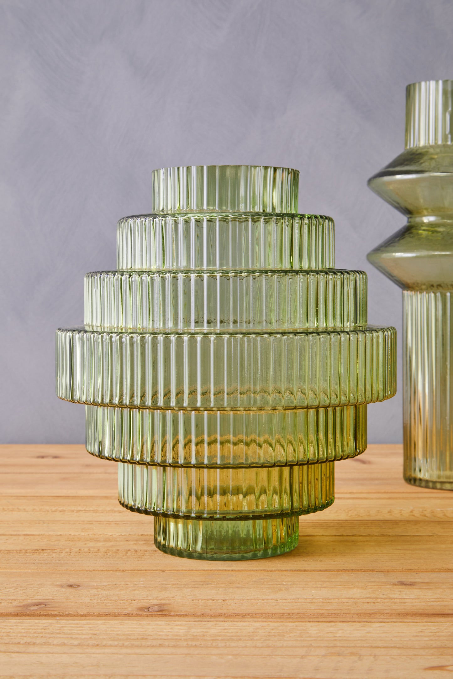 Green glass vase with ribbed texture on a wooden surface against a gray background
