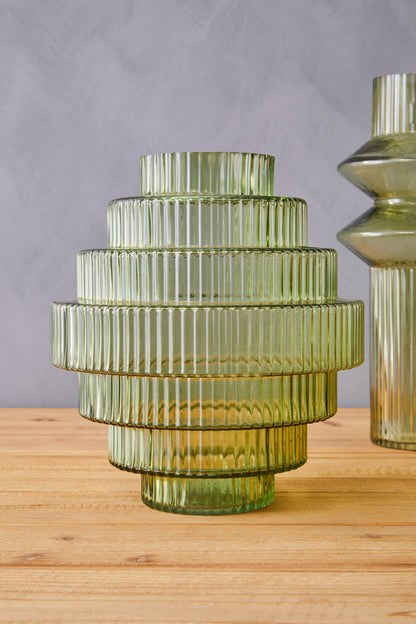 Green glass vase with ribbed texture on a wooden surface against a gray background