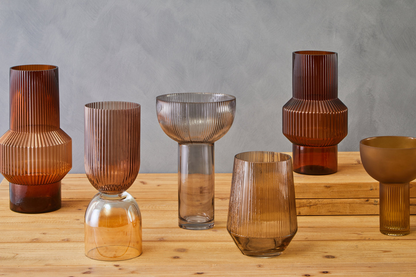 Set of brown glass vases on a wooden surface with a gray background
