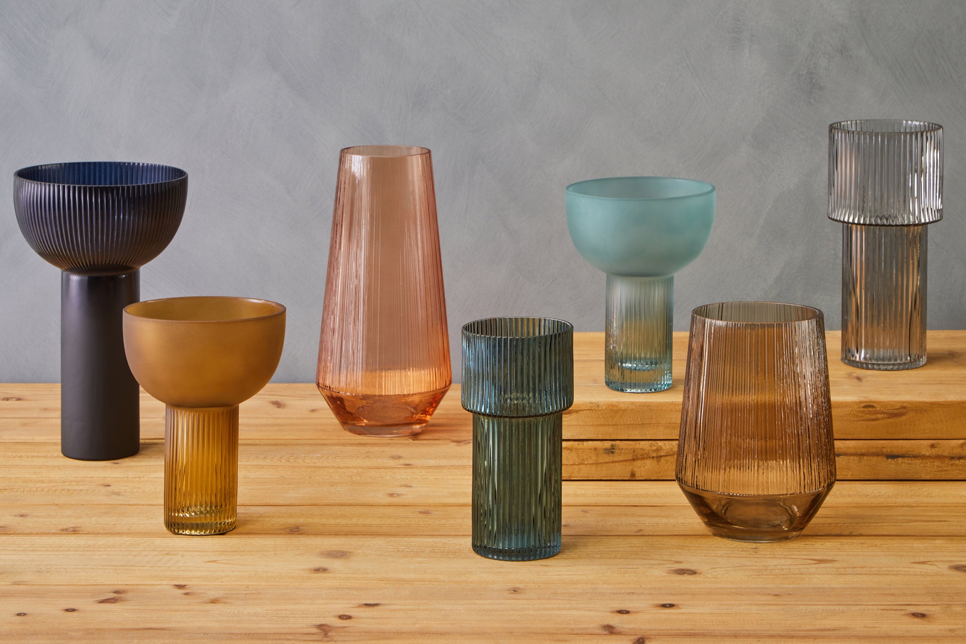 Set of colorful glass vases on a wooden surface with a gray background