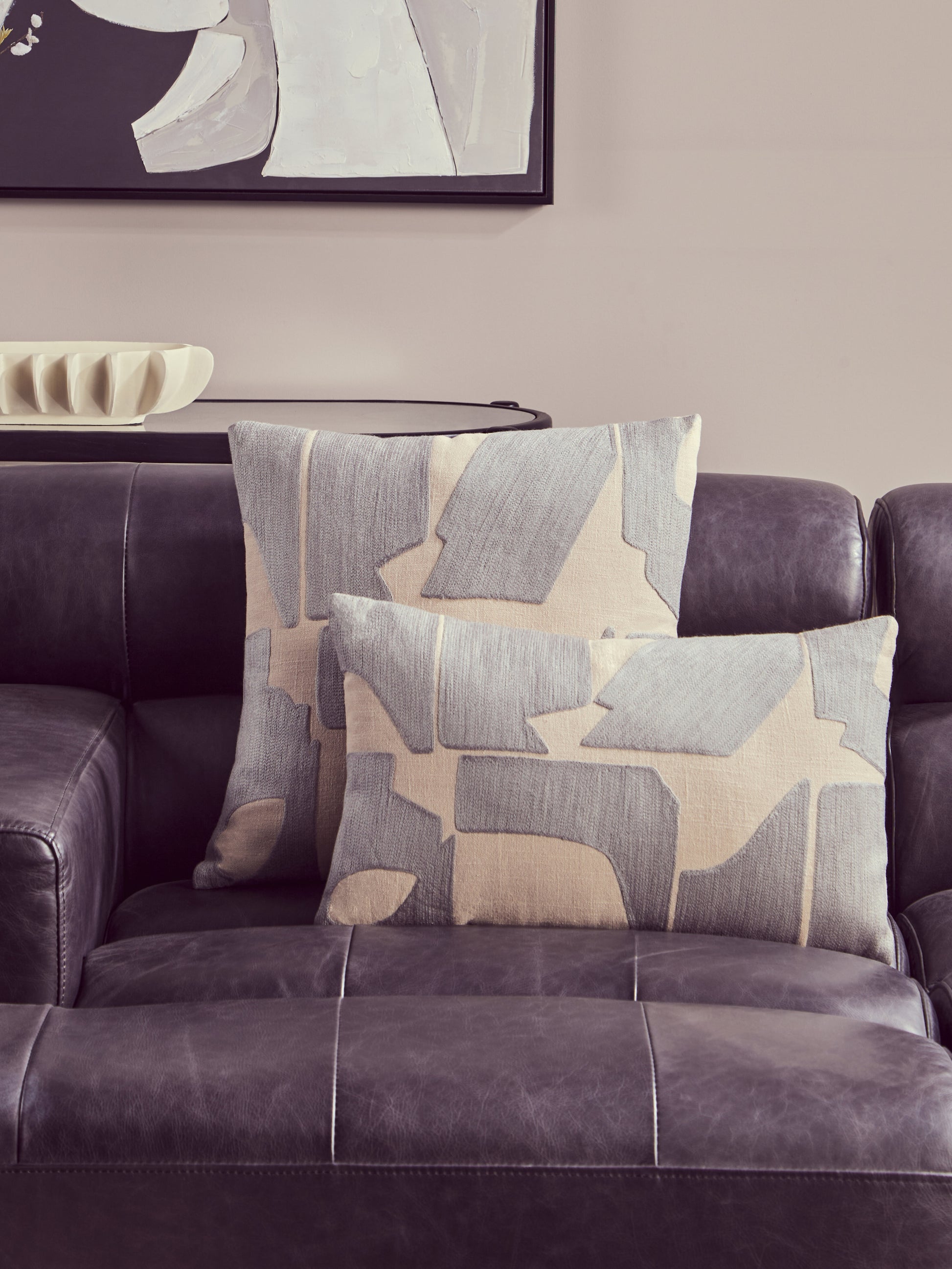 Gray and beige patterned pillows on a sofa with abstract art in the background.